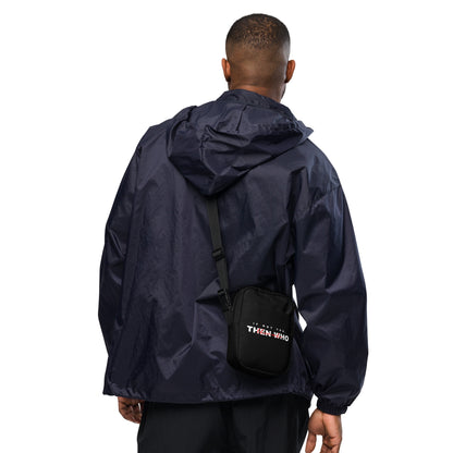 Person wearing a navy raincoat with a black bag featuring 'THEN WHO' branding on a white background